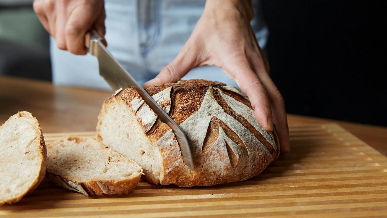 Frisches Brot wird auf einem bulthaup Brotschneidebrett aufgeschnitten.