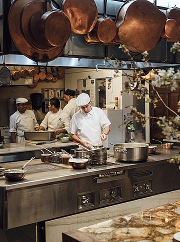 Aufnahme von vier Köchen in der Küche, über den Kücheninseln hängen diverse Kupfertöpfe aus Bouley's Sammlung